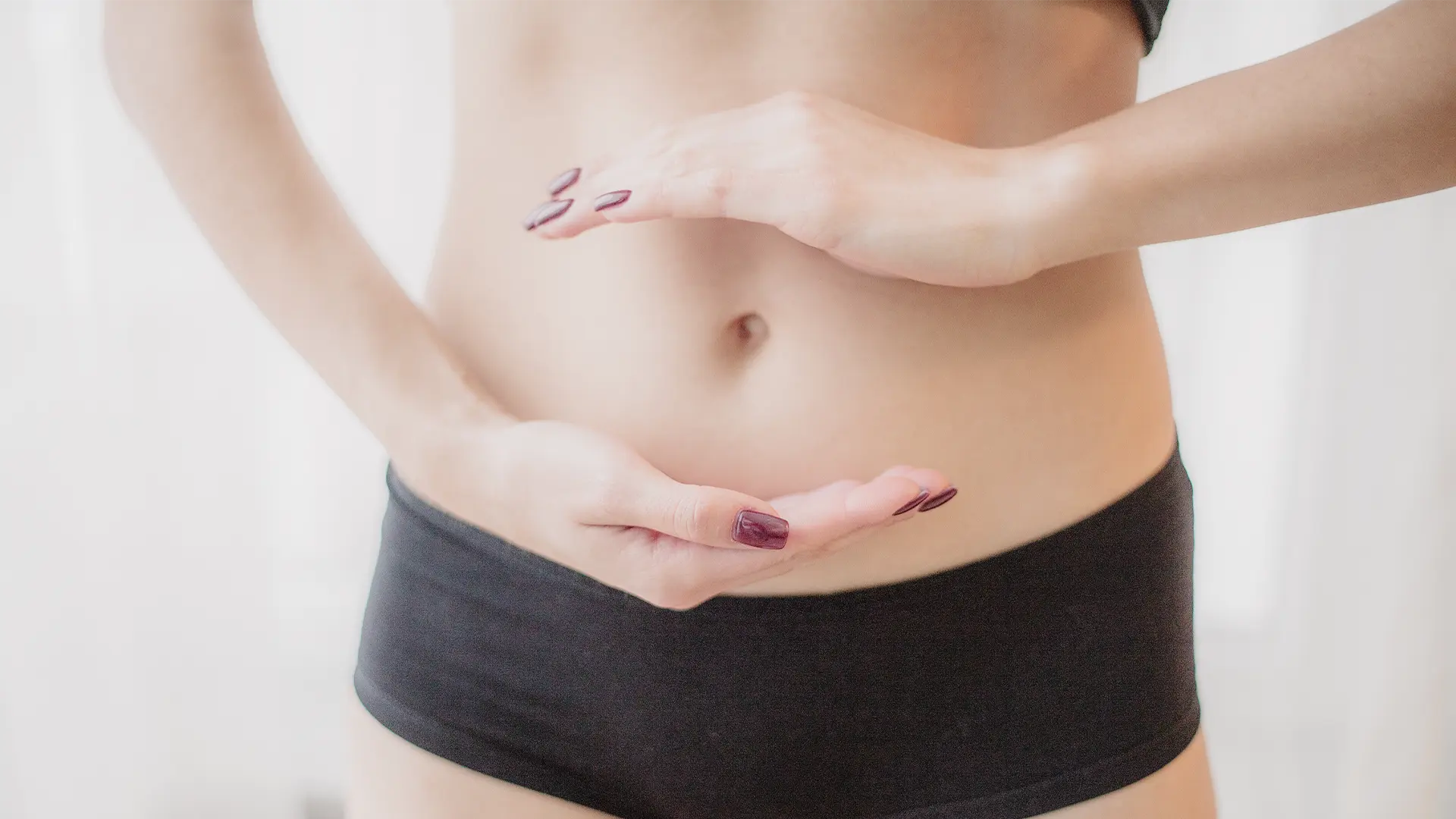 Hände einer Frau formen schützend einen Kreis auf ihrem Bauch
