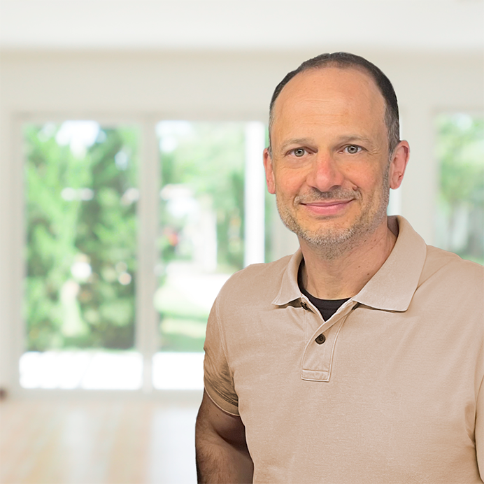 Unser Experte Markus Weingärtner im Portait Unser rubyni Experte, Heilpraktiker und Therapeut Markus Weingärtner blickt freundlich in die Kamera. Er trägt ein beiges Polo-Shirt und steht in einem hellen Raum. Im Hintergrund sieht man Fenster, die auf einen Garten hinausgehen.