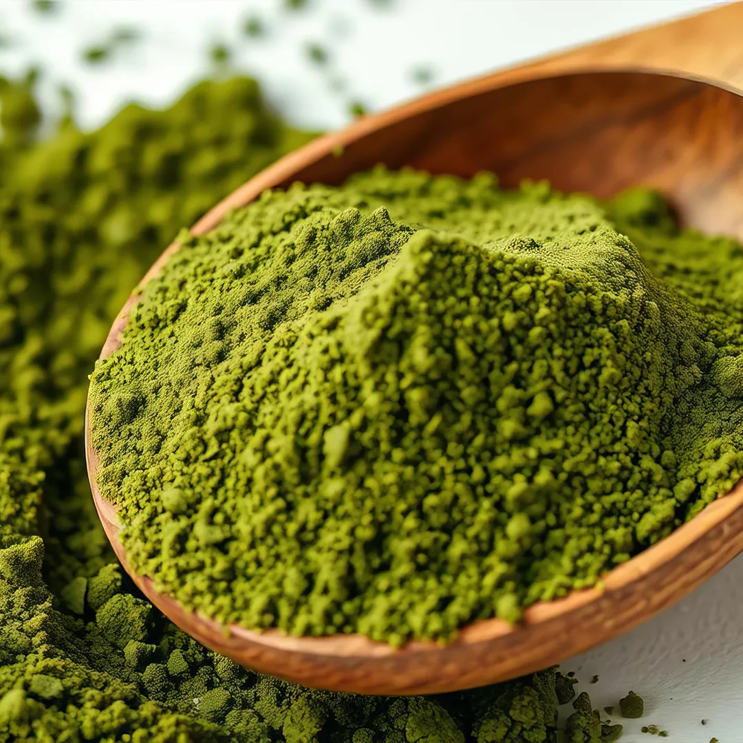 rubyni® Vitamin D – das Multitalent für eine gute Gesundheit Grünalgenpulver in einem Holzlöffel auf einem weißen Tisch. Auf dem Tisch ist auch jede Menge ausgeschüttetes grünes Pulver.