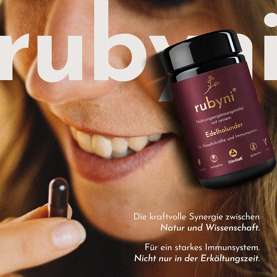 rubyni® Holunder im Glas vor einem Frauengesicht. Man sieht den Mund in Großaufnahme, er ist leicht geöffnet und die Frau hält eine rote Kapsel vor den Mund.