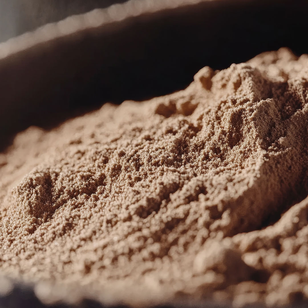 Man sieht einen Ausschnitt einer Holzschale, in der sich braunes Pulver befindet.