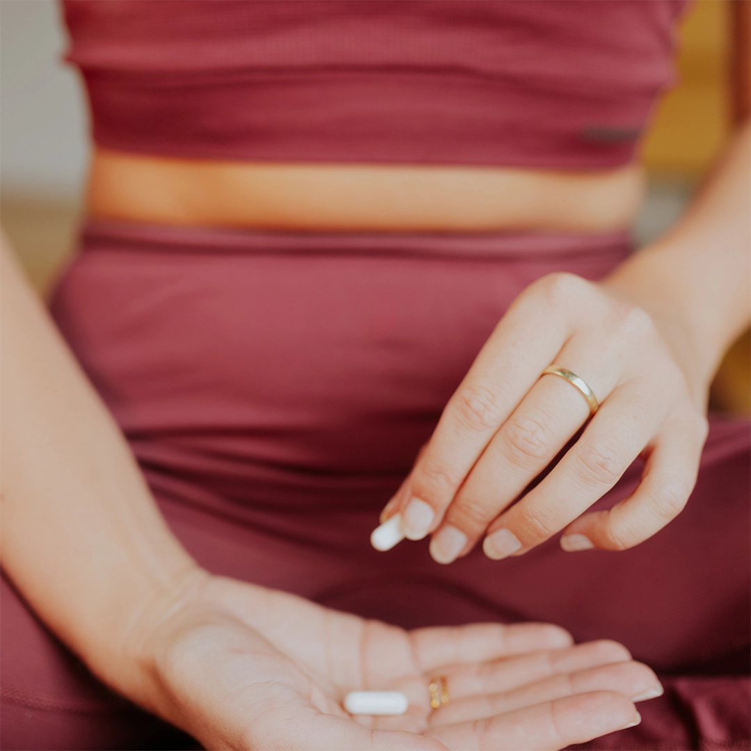 Eine Frau hält eine Kapsel zwischen den Fingern und lässt sie in ihre geöffnete Hand gleiten, während die ruhige, bewusste Geste den Moment der täglichen Ergänzung und achtsamen Selbstfürsorge widerspiegelt.