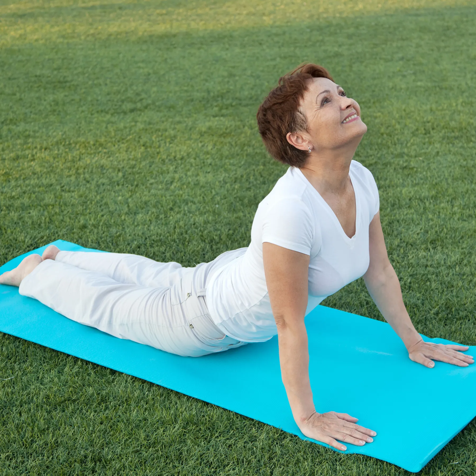 Eine Frau führt eine Dehnübung im Freien aus. Sie wirkt konzentriert und entspannt, während sie ihren Körper bewusst streckt. Die natürliche Umgebung und das weiche Licht unterstreichen ein aktives, gesundheitsbewusstes Lebensgefühl.