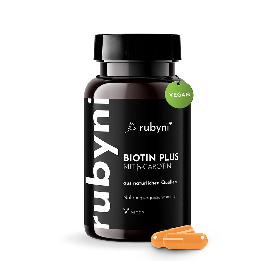 Foto zur Illustration des Produkts PET-Dose des rubyni Nahrungsergänzungsmittels „Biotin Plus“ mit β-Carotin sowie zwei orangefarbene Kapseln davor auf hellem Hintergrund.