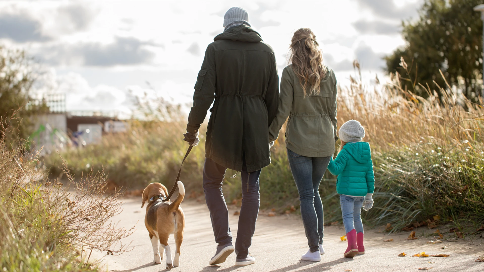 Familie mit Kind und Hund spaziert gemeinsam auf einem Weg durch die Natur bei warmem Tageslicht.