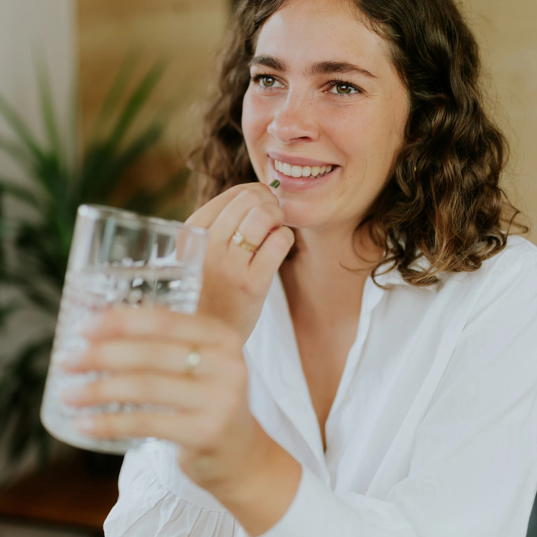 Frau nimmt eine Kapsel ein und hält dazu ein Glas Wasser in der Hand.
